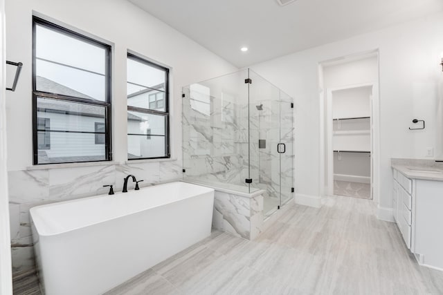 bathroom with recessed lighting, vanity, a marble finish shower, a walk in closet, and a freestanding bath