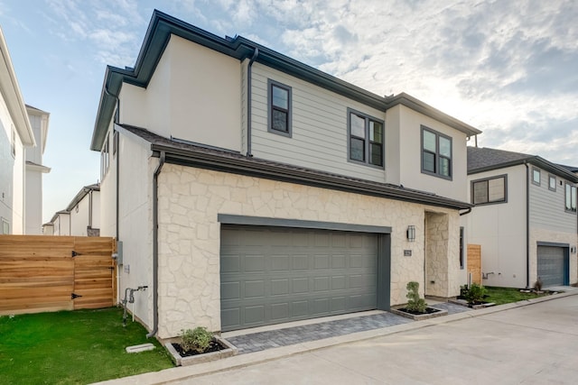 view of front of house with fence, driveway, an attached garage, and stone siding