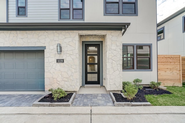 view of exterior entry with a garage, stone siding, stucco siding, and fence