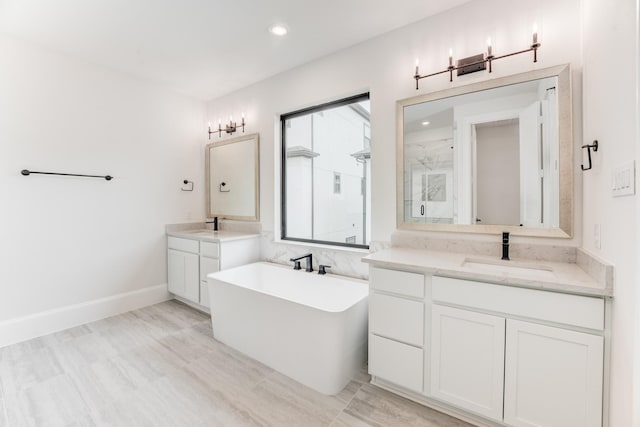 full bath featuring recessed lighting, two vanities, a freestanding tub, a sink, and a marble finish shower