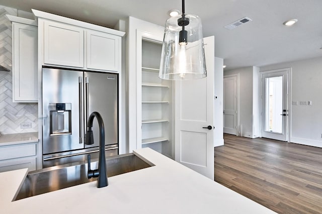 kitchen featuring high end refrigerator, decorative backsplash, visible vents, light countertops, and wood finished floors