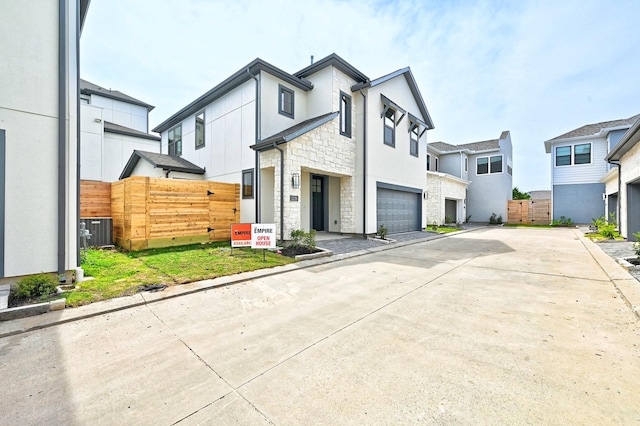 contemporary home featuring driveway, stone siding, fence, central AC, and a garage