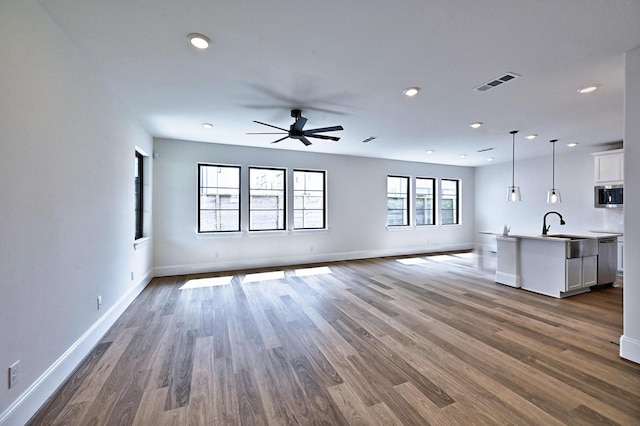 unfurnished living room with baseboards, visible vents, wood finished floors, and ceiling fan