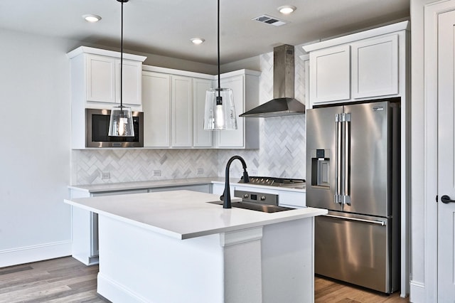 kitchen with a sink, appliances with stainless steel finishes, visible vents, light wood-style floors, and wall chimney exhaust hood