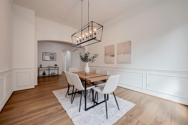 dining area featuring wainscoting, arched walkways, light wood finished floors, and a decorative wall