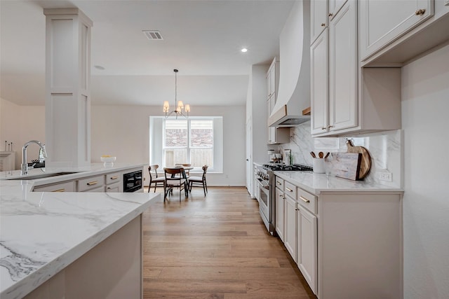 kitchen featuring high end stove, a sink, a chandelier, light stone countertops, and light wood finished floors