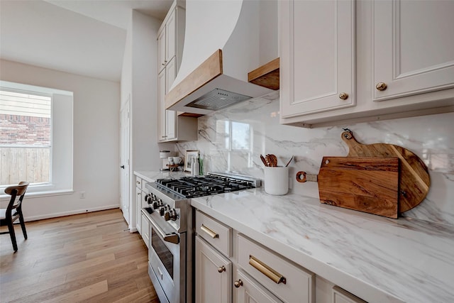 kitchen with light wood-type flooring, custom exhaust hood, tasteful backsplash, high end stainless steel range, and light stone counters
