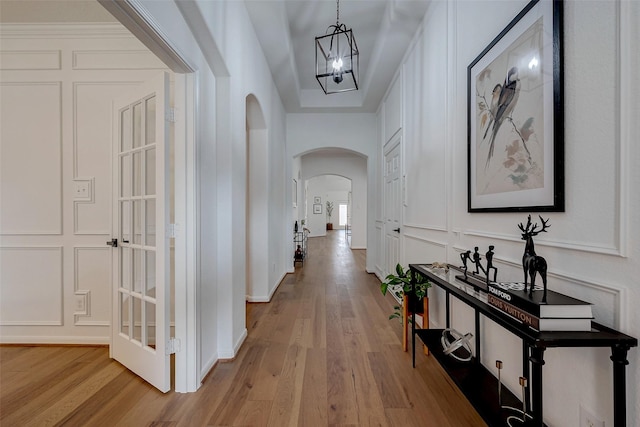 hallway with arched walkways, a notable chandelier, light wood-style floors, and a decorative wall