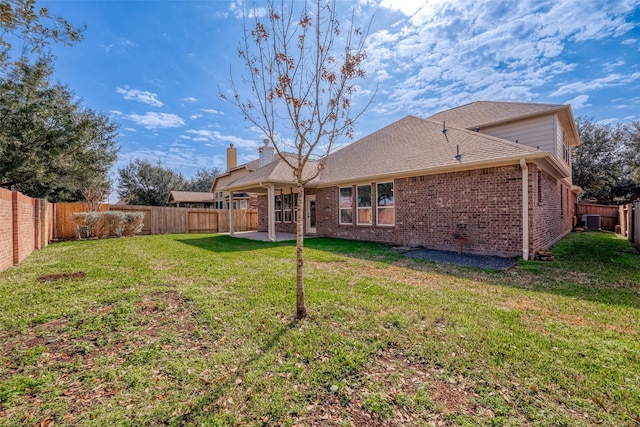 back of property featuring brick siding, a fenced backyard, a shingled roof, and a yard
