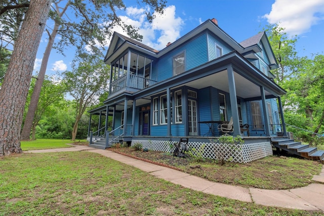 view of side of property with covered porch, a balcony, and a yard