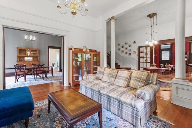 living area featuring wood finished floors, stairway, decorative columns, and a chandelier