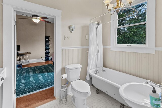 bathroom featuring wainscoting, ceiling fan with notable chandelier, toilet, a sink, and a soaking tub