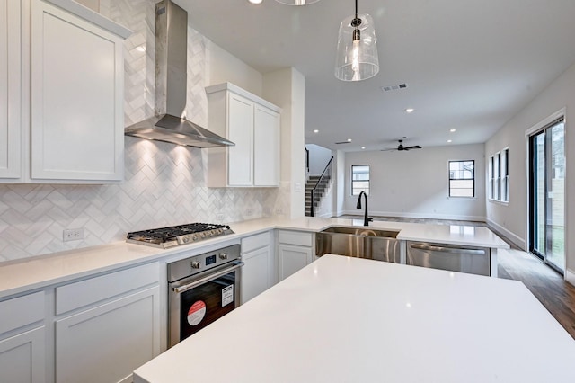 kitchen with stainless steel appliances, a wealth of natural light, wall chimney range hood, ceiling fan, and visible vents