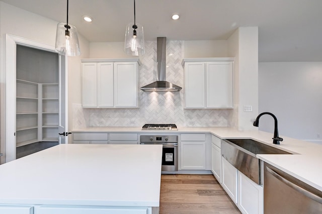 kitchen featuring tasteful backsplash, stainless steel appliances, a sink, white cabinetry, and wall chimney exhaust hood
