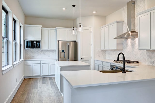 kitchen featuring appliances with stainless steel finishes, light countertops, light wood finished floors, a center island, and wall chimney exhaust hood