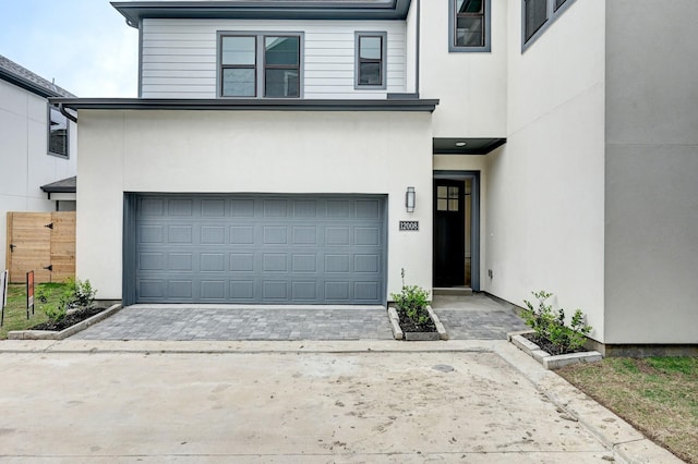 view of front of home featuring stucco siding, fence, driveway, and a garage