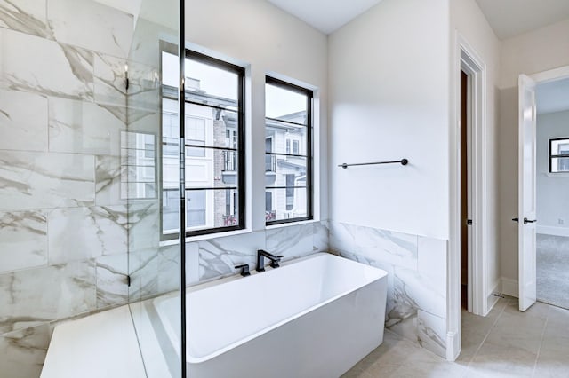 bathroom with a soaking tub, tile walls, and plenty of natural light