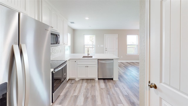 kitchen featuring white cabinets, stainless steel appliances, a peninsula, and light wood finished floors