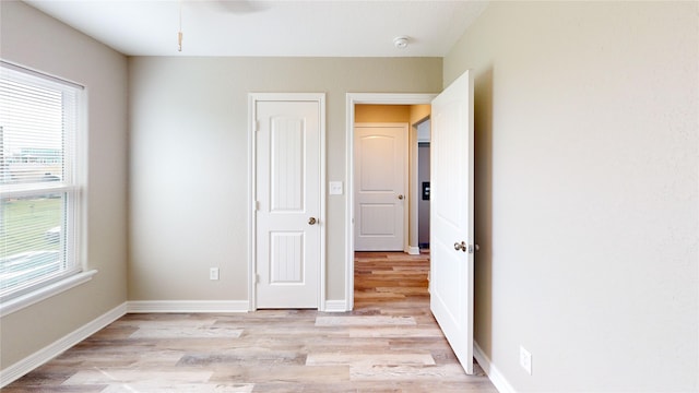 unfurnished bedroom featuring multiple windows, baseboards, and light wood-type flooring