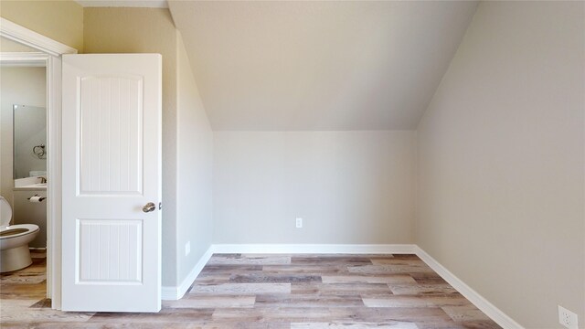 additional living space with baseboards, light wood-type flooring, and vaulted ceiling