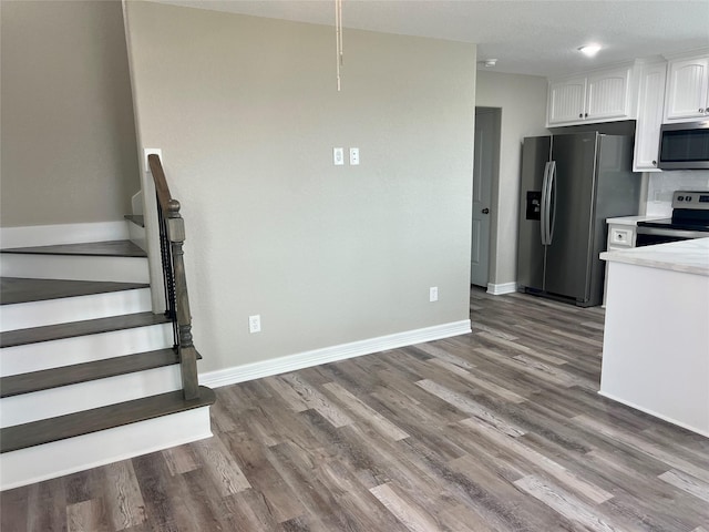kitchen with white cabinets, stainless steel appliances, light countertops, baseboards, and wood finished floors
