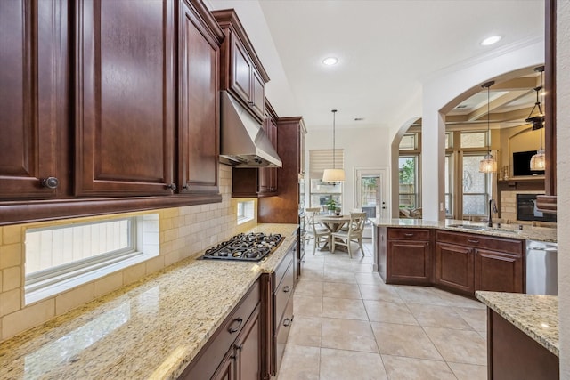 kitchen with arched walkways, under cabinet range hood, a sink, appliances with stainless steel finishes, and backsplash