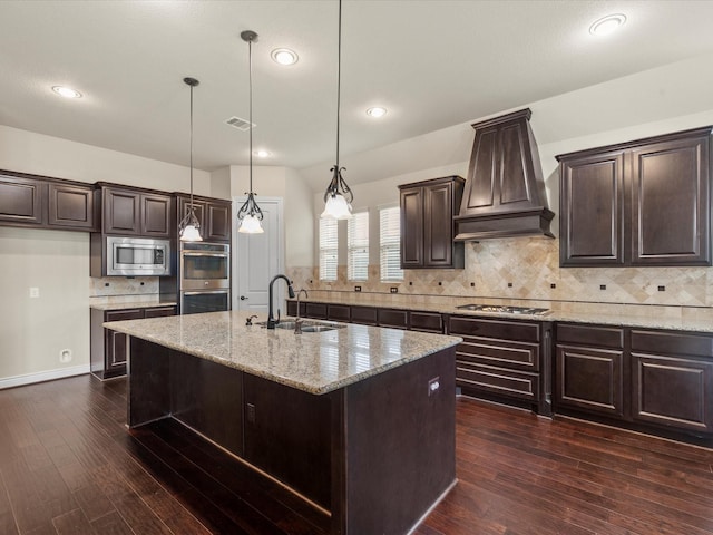 kitchen with dark brown cabinetry, visible vents, appliances with stainless steel finishes, a sink, and custom exhaust hood