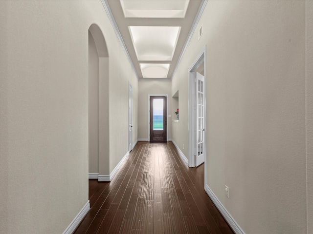 corridor featuring arched walkways, baseboards, and dark wood-style flooring