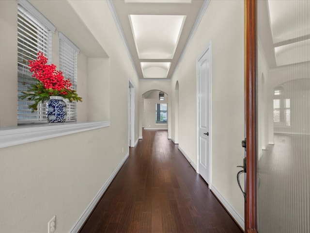 corridor featuring arched walkways, baseboards, and wood finished floors