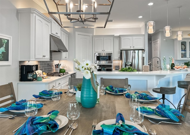 kitchen featuring stainless steel appliances, under cabinet range hood, backsplash, a notable chandelier, and crown molding