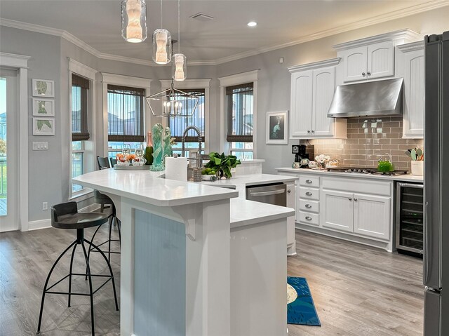 kitchen with beverage cooler, under cabinet range hood, an inviting chandelier, light wood finished floors, and an island with sink