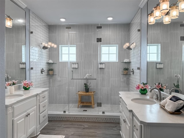 bathroom featuring two vanities, a tile shower, wood finished floors, and a sink