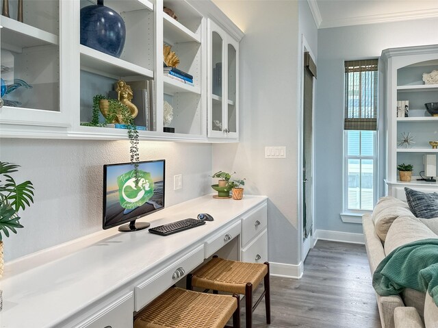 office space featuring built in desk, baseboards, ornamental molding, and dark wood finished floors