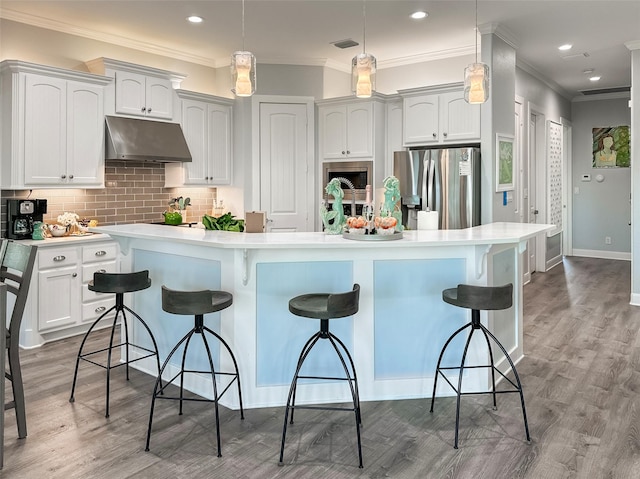kitchen featuring a breakfast bar, stainless steel fridge, under cabinet range hood, visible vents, and crown molding