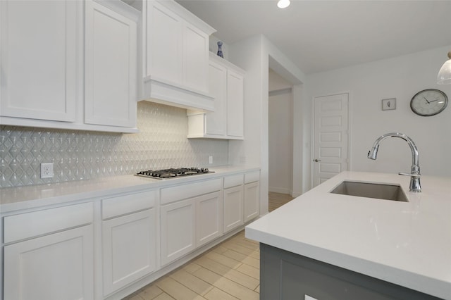 kitchen with decorative backsplash, white cabinets, a sink, light countertops, and stainless steel gas cooktop