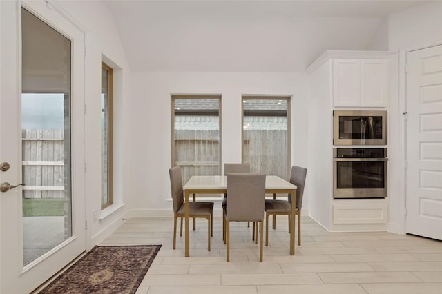 dining area featuring baseboards, a wealth of natural light, lofted ceiling, and light wood-type flooring