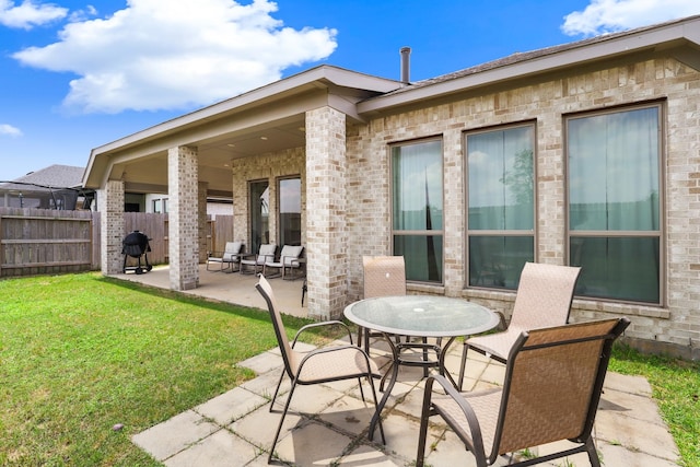rear view of house featuring fence, a lawn, a patio, and brick siding