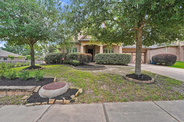 view of property hidden behind natural elements featuring fence, an attached garage, concrete driveway, and brick siding