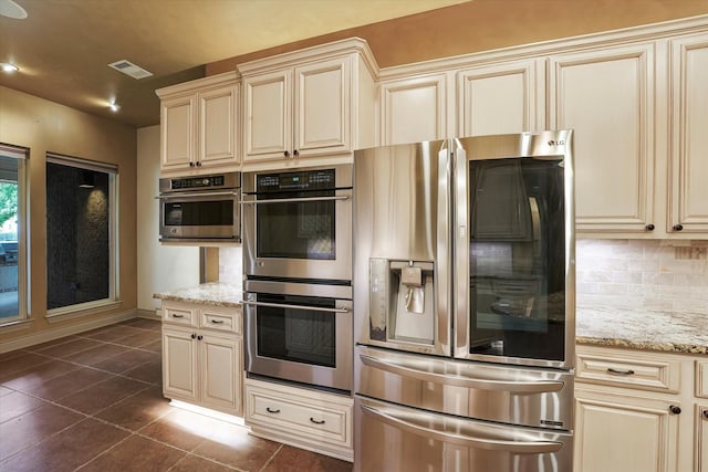kitchen featuring visible vents, cream cabinetry, dark tile patterned flooring, tasteful backsplash, and stainless steel appliances