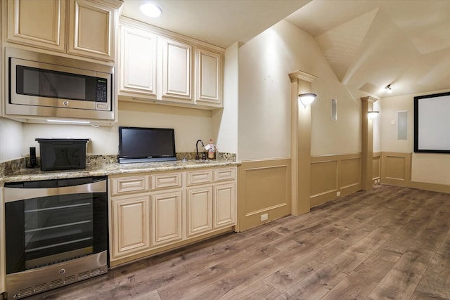 bar featuring light wood-style floors, wainscoting, vaulted ceiling, stainless steel microwave, and wine cooler