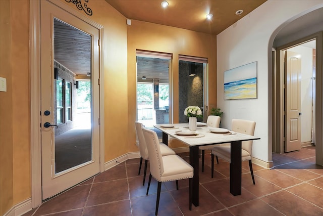 dining space with dark tile patterned floors, baseboards, and arched walkways