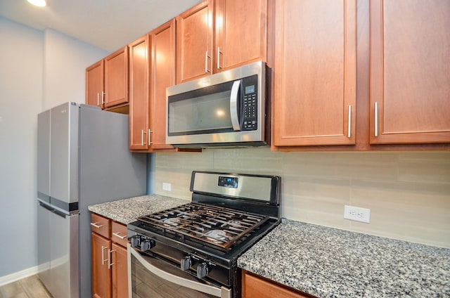 kitchen featuring tasteful backsplash, wood finished floors, light stone countertops, and appliances with stainless steel finishes