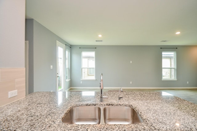 kitchen featuring light stone counters, open floor plan, a healthy amount of sunlight, and a sink