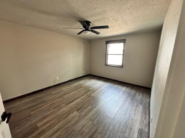 empty room with dark wood-style floors, baseboards, ceiling fan, and a textured ceiling
