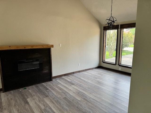 unfurnished living room featuring lofted ceiling, a chandelier, wood finished floors, and a glass covered fireplace