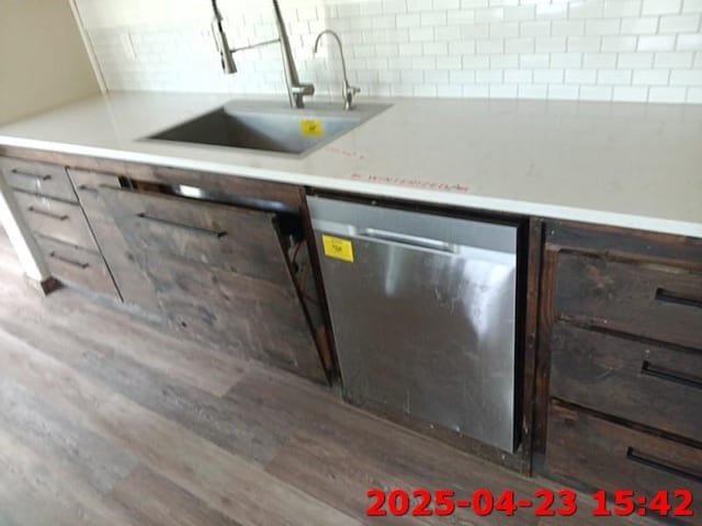 kitchen featuring a sink, decorative backsplash, light countertops, stainless steel dishwasher, and wood finished floors