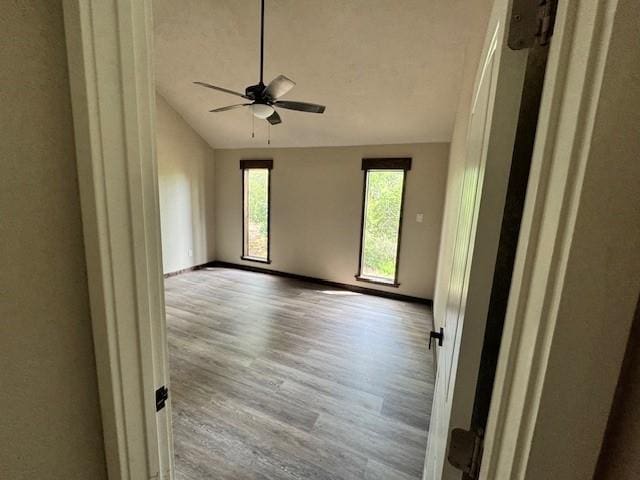 spare room with wood finished floors, ceiling fan, vaulted ceiling, and baseboards