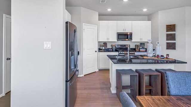 kitchen with a sink, a kitchen breakfast bar, white cabinetry, appliances with stainless steel finishes, and wood finished floors