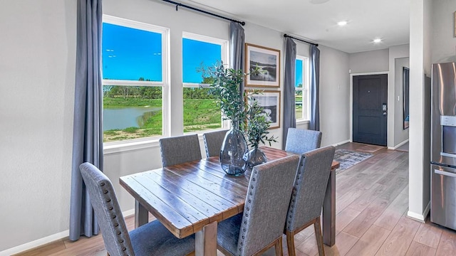 dining space with baseboards, a healthy amount of sunlight, light wood-style floors, and a water view