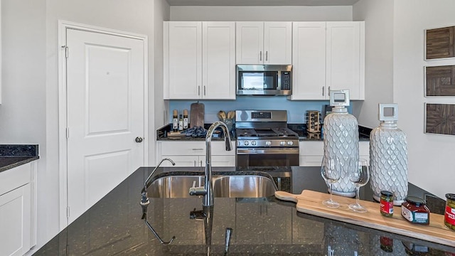 kitchen with white cabinetry, dark stone countertops, appliances with stainless steel finishes, and a sink
